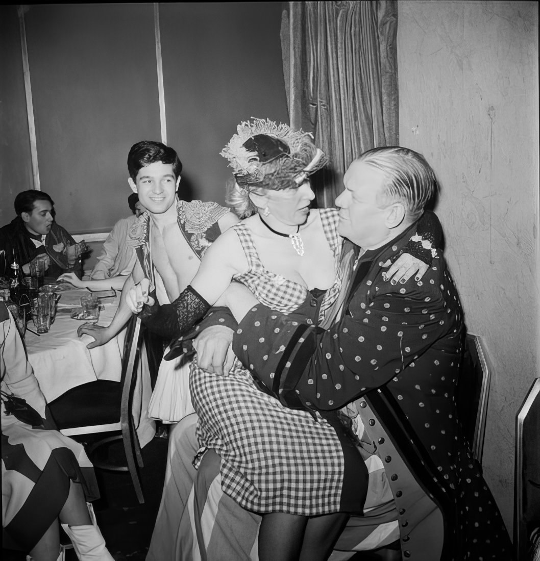 A woman sitting on a man's lap as another man looks on, 1951.