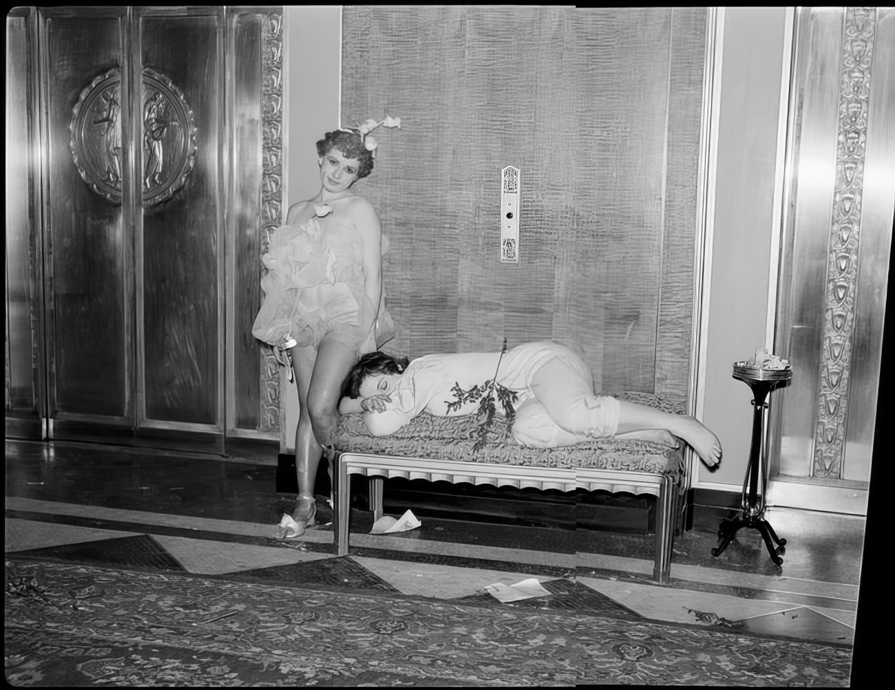 A woman waiting for the elevator by a small couch where a woman is sleeping, 1951.