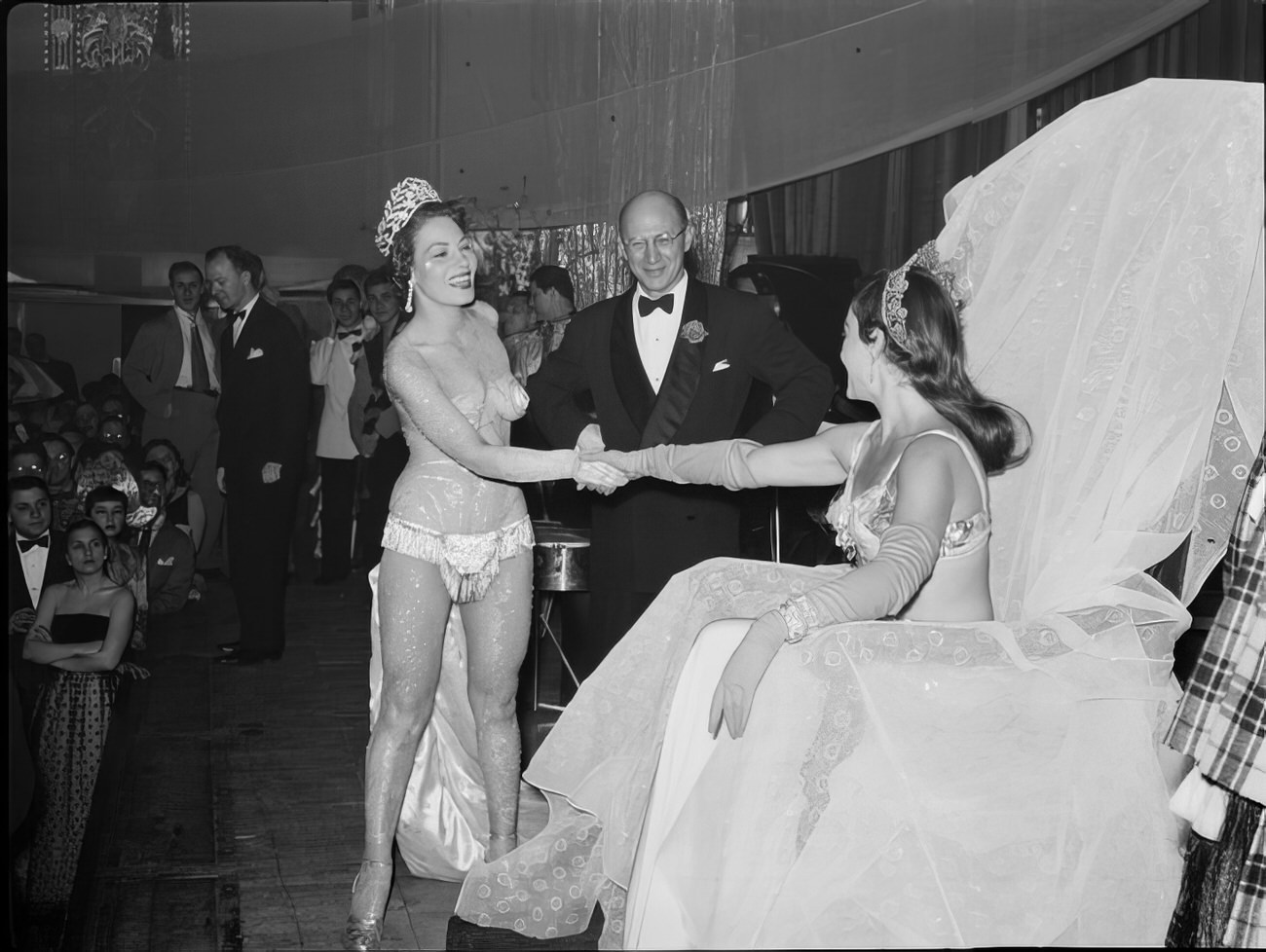 Women shaking hands on stage as a man looks on, 1951.