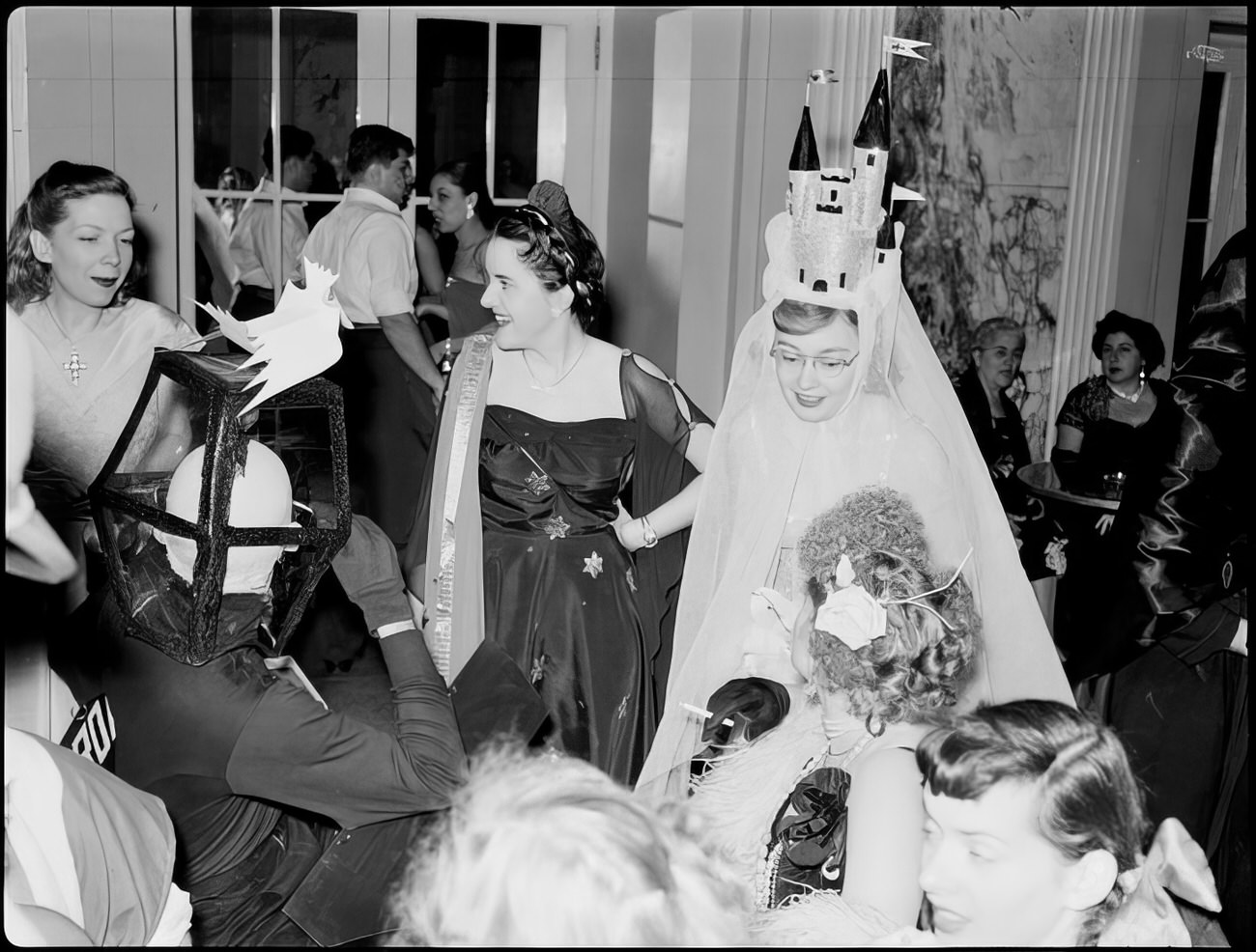 A group of guests in elaborate costumes talking, 1951.