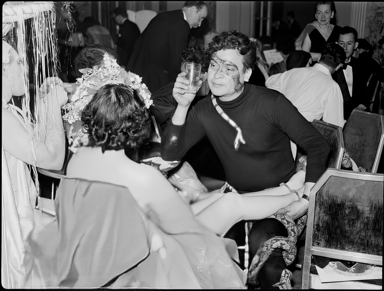 A man with fake snakes attached to him talking to a woman, 1951.