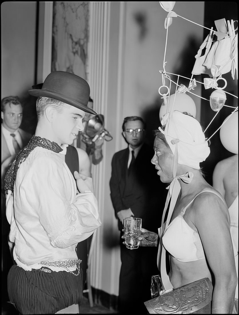 A woman with an elaborate headpiece talking to a man, 1951.