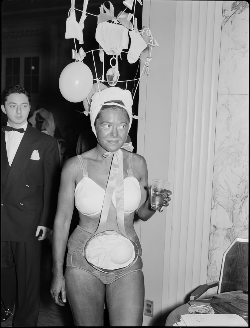 A woman with an ornate headpiece holding a drink, 1951.