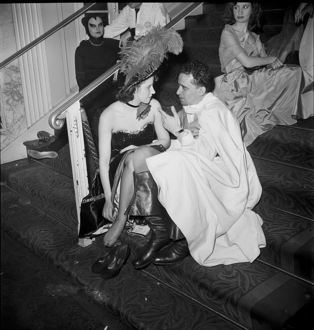 Costumed ball guests sitting and talking on steps, 1951.