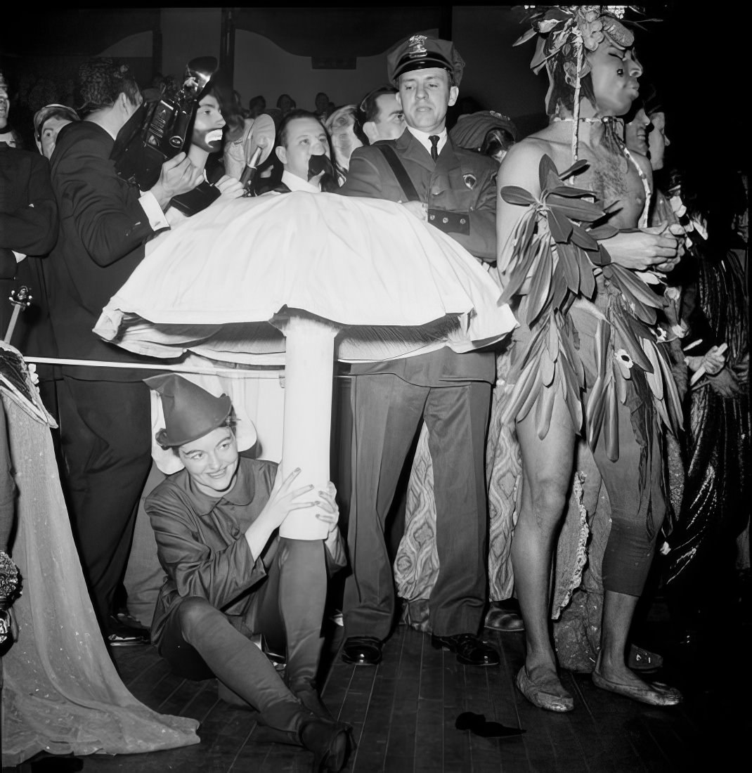 Costumed ball guests, one under a model of a mushroom, 1951.