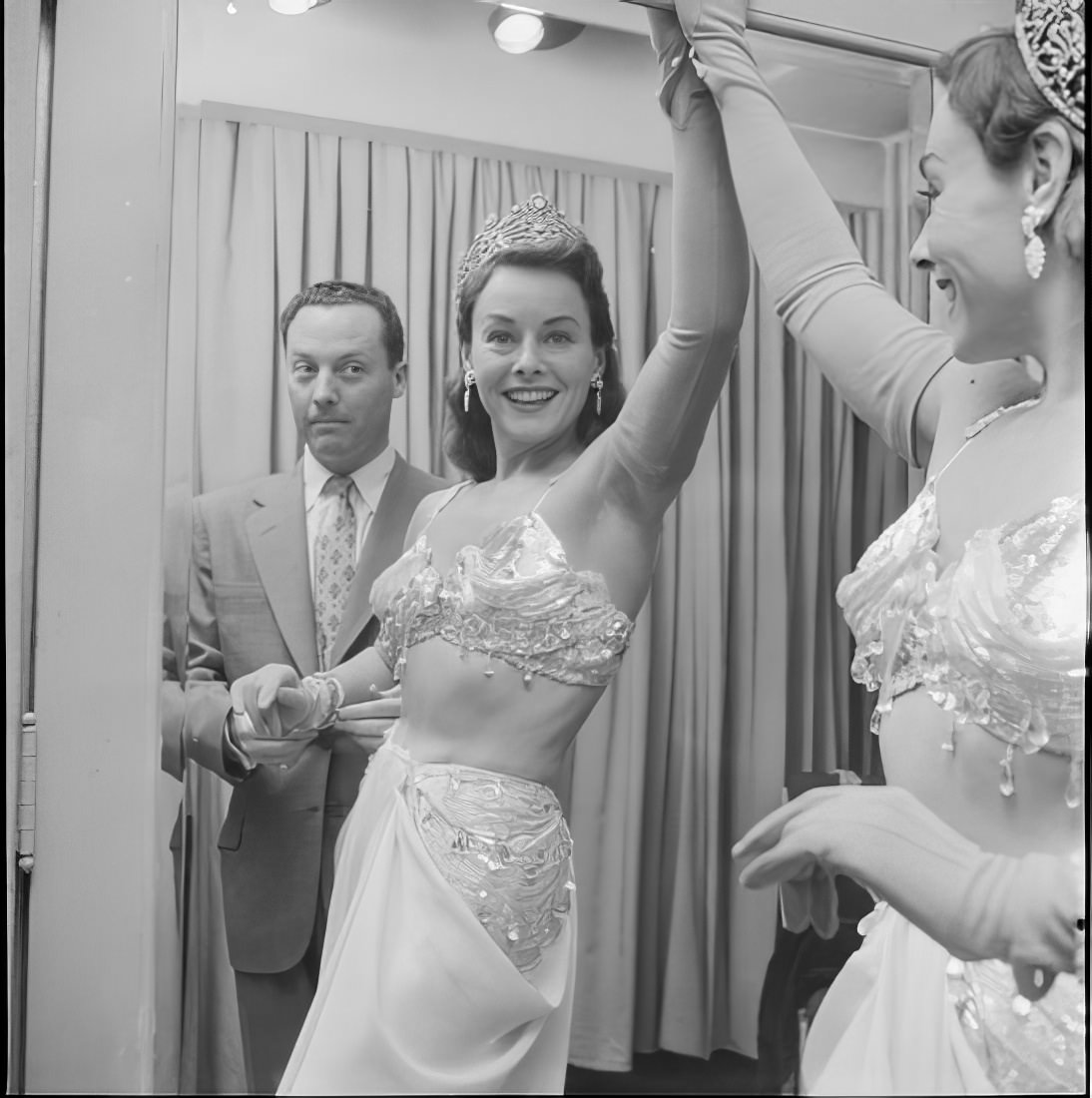 A costumed woman posing in a mirror as a man watches, 1951.