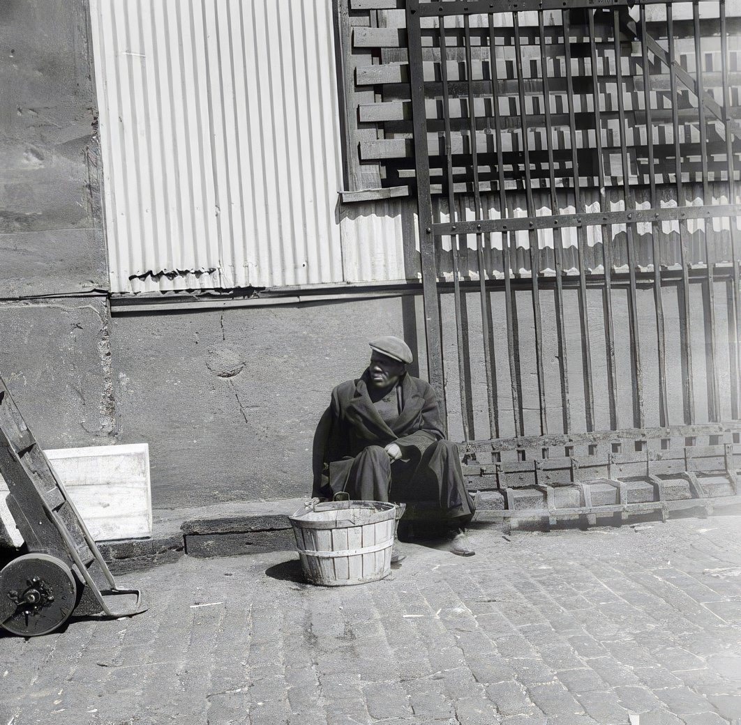 Waterfront scene with a man seated on a curb, 1937.