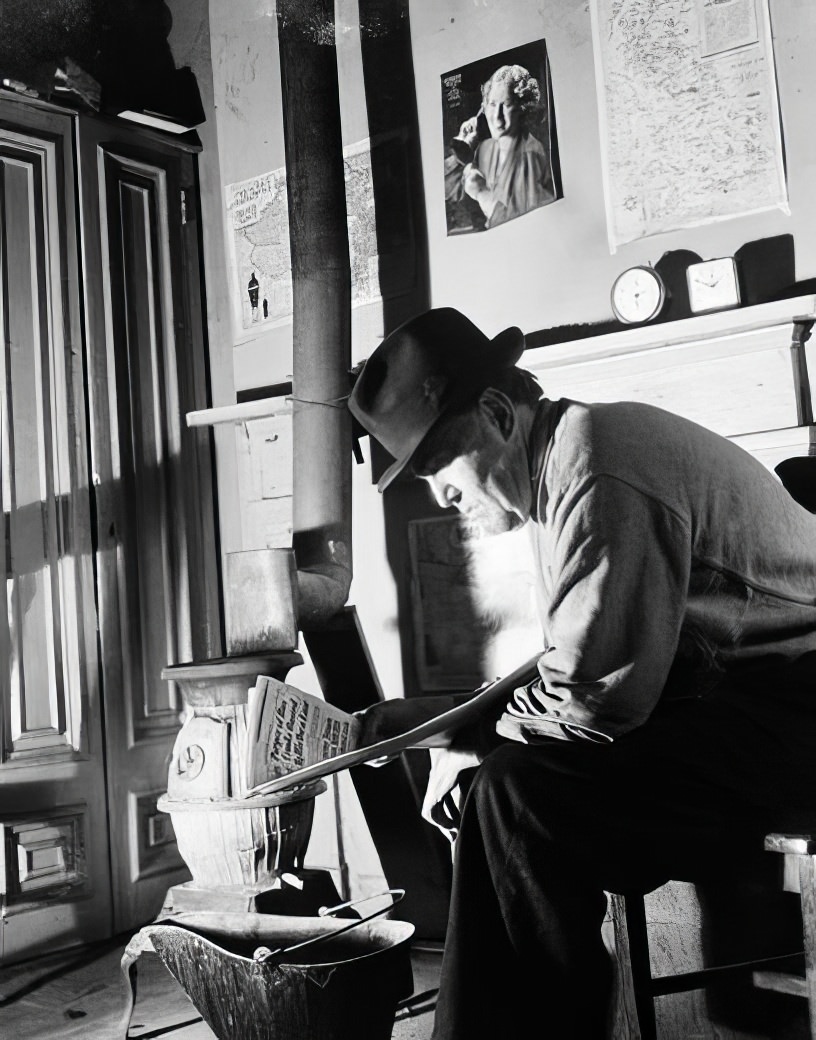 Man reading near a pot-bellied stove, 1936.