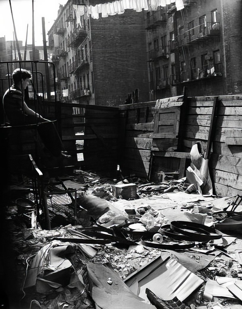 Boy on fire escape above a littered lot, 1936