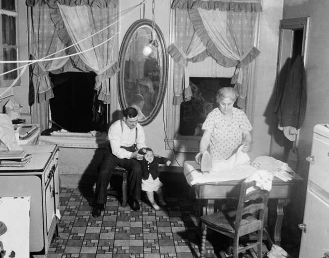 Kitchen interior: Father, baby, and mother ironing, 1935.