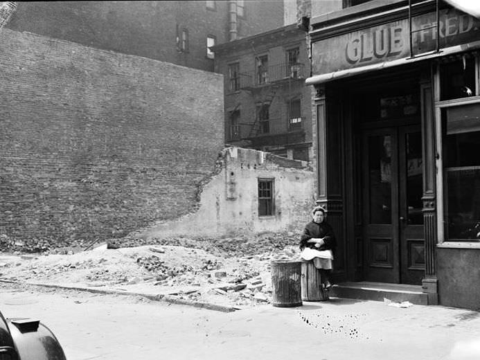 Woman sitting on a garbage can next to a vacant lot, 1935.