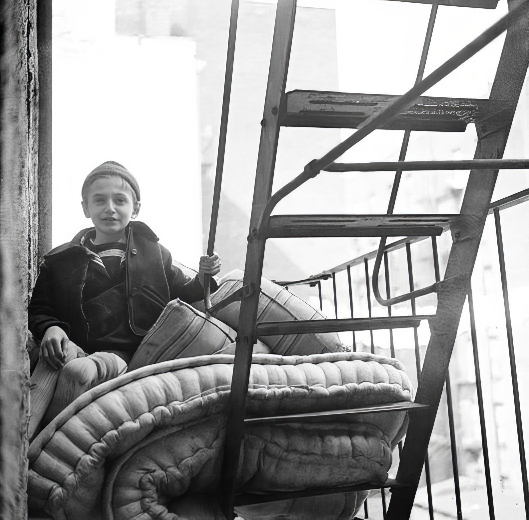 Boy on fire escape with mattress, 1936.