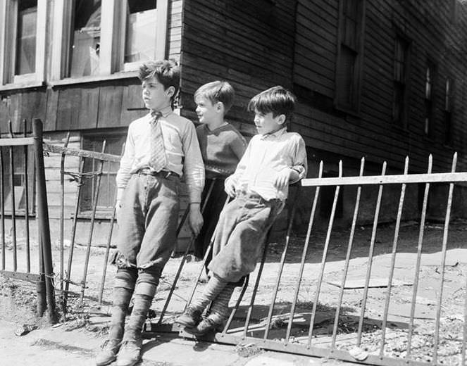 Three boys leaning on an iron fence, 1936.