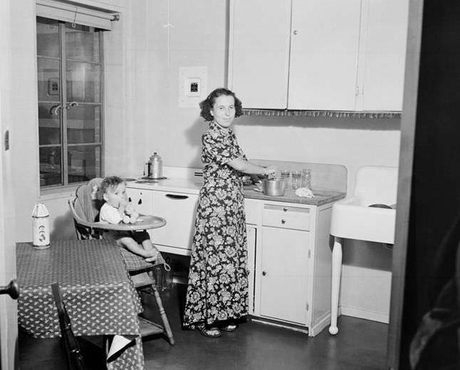 Mother at stove, baby in highchair, 1935.