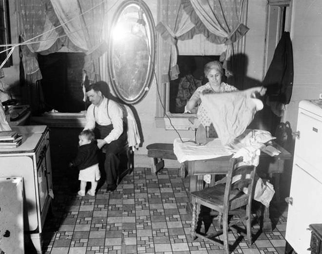 Kitchen interior: woman ironing, man with child, 1935.