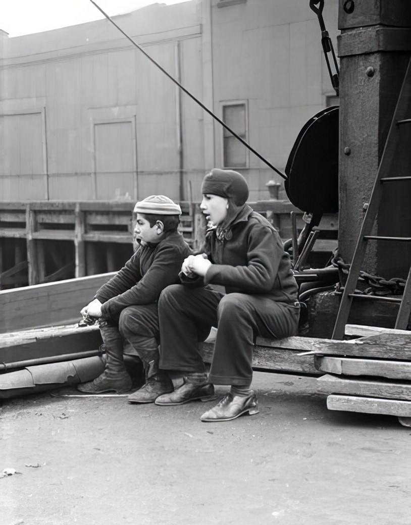 Waterfront scene: boys sitting on a wharf, May 1937.