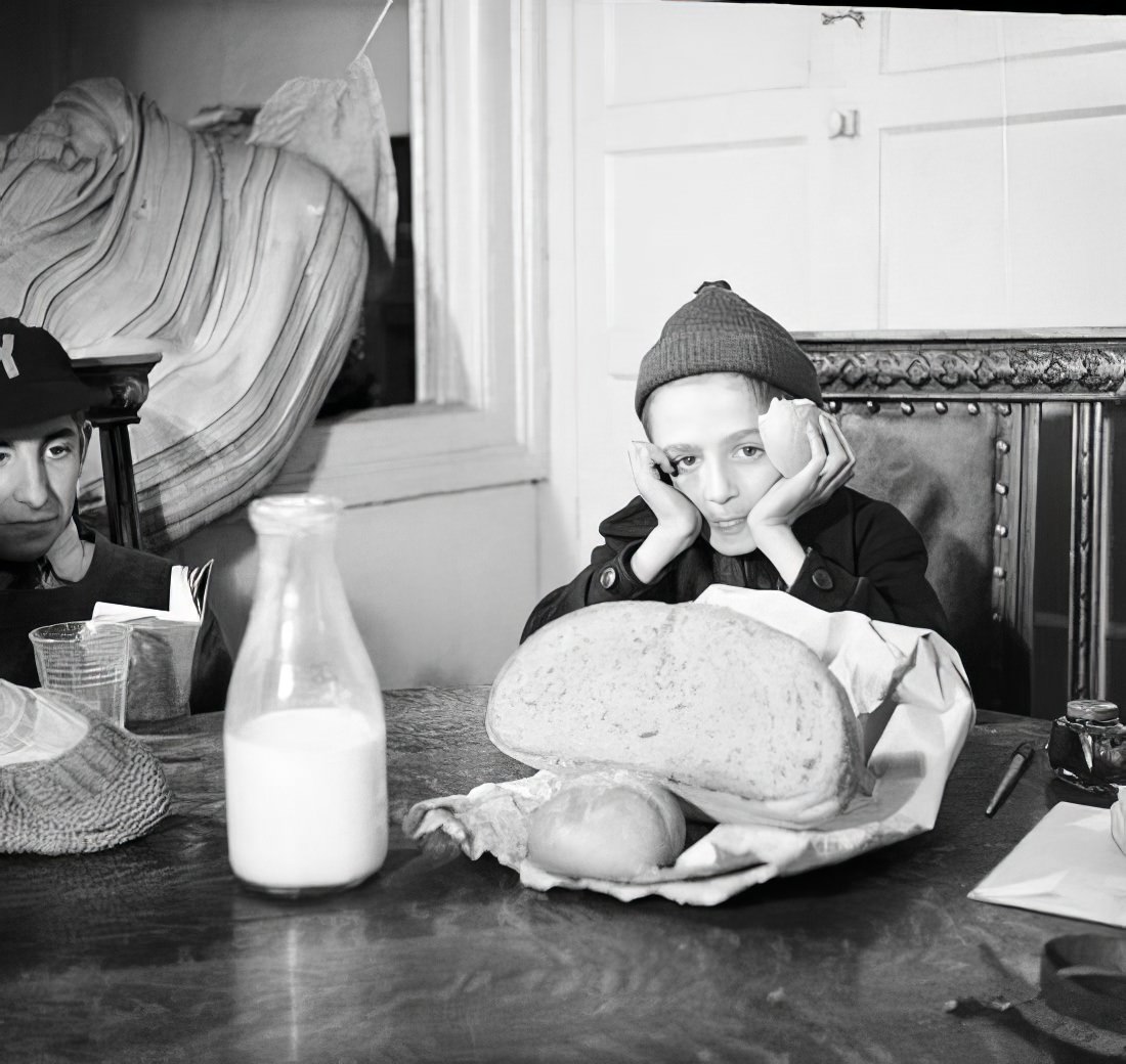 Boy at a table with a milk bottle and bag, 1935.