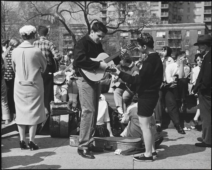 A female guitarist in shorts and sneakers with other musicians in Washington Square Park, 1956.