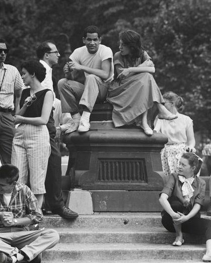 A girl in a polka dot blouse watching the crowd on the fountain steps, Washington Square Park, 1956.