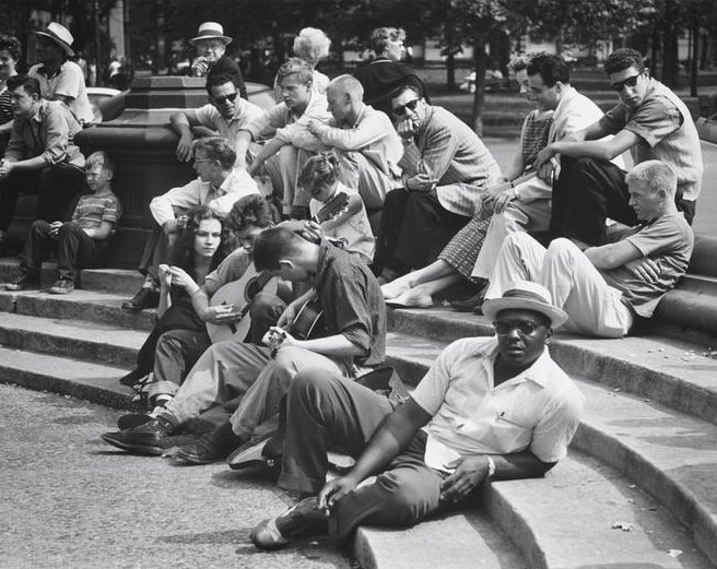 A Black man with a brimmed hat sitting with musicians on the fountain steps, Washington Square Park, 1956.