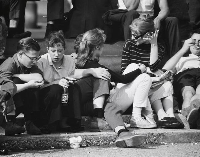 A girl in a crowd drinking Pepsi Cola on the fountain steps, Washington Square Park, 1956.