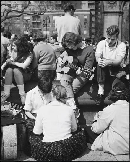 A girl playing the guitar, with three girls in the background, Washington Square Park, 1956.