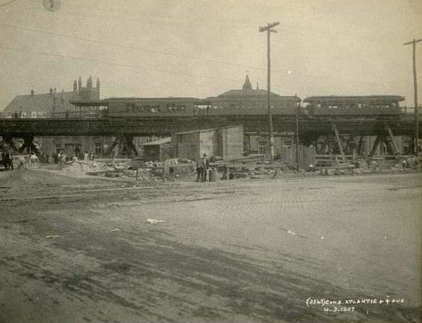 View of subway construction site at the intersection of Atlantic Avenue and 4th Avenue. Image includes three trolley cars at an elevated station in the background, 1907.