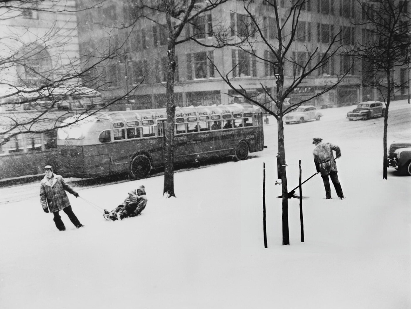 New York Parks Department employee Joseph Giglio clears snow on Central Park Plaza as a man pulls children on a sled, 1948.