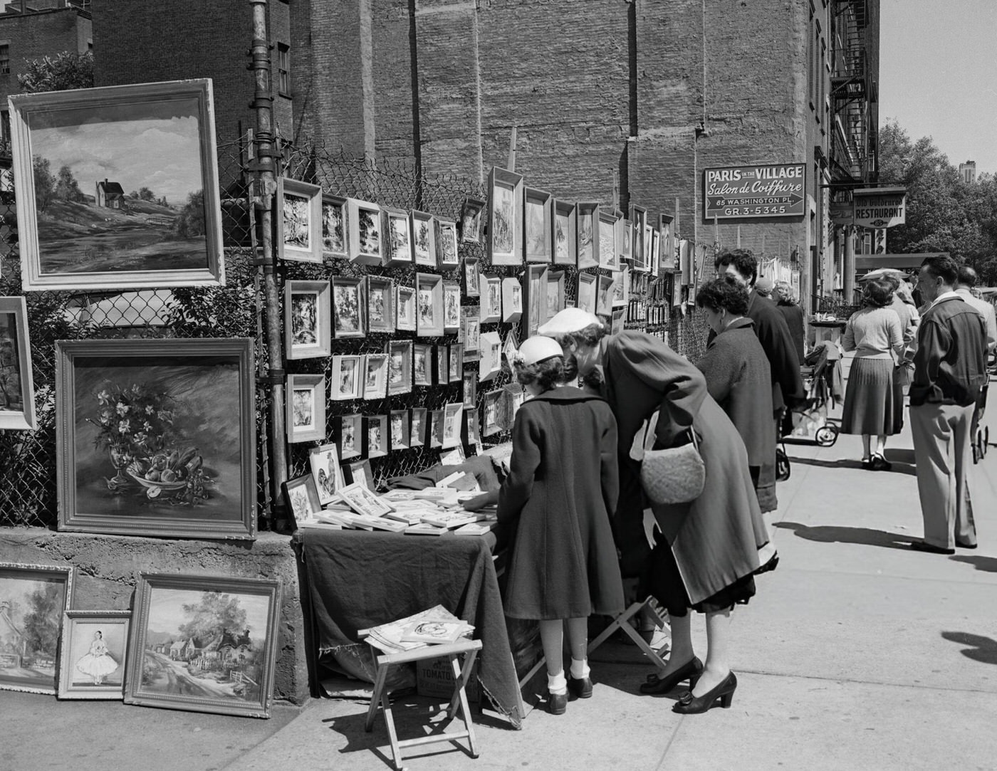 Potential customers admire paintings at a sidewalk art show in Greenwich Village.