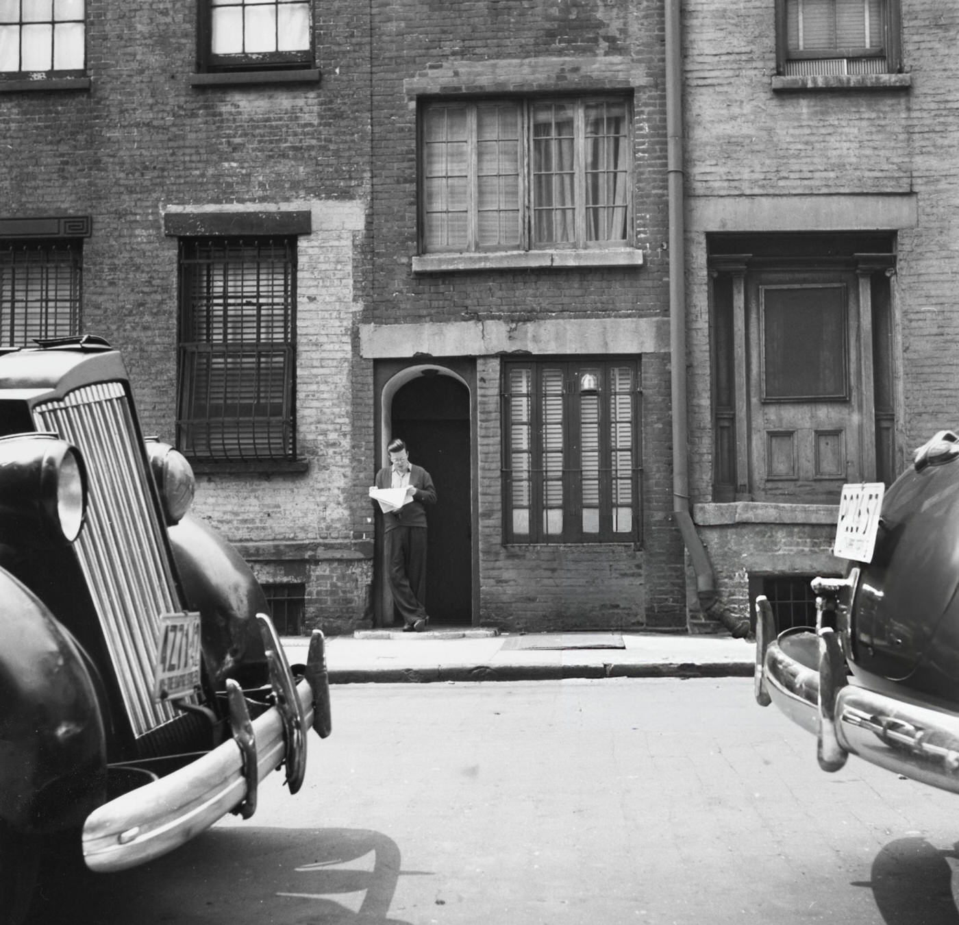 A man reads a newspaper in the doorway of 75½ Bedford Street, the narrowest townhouse in New York City, 1951.