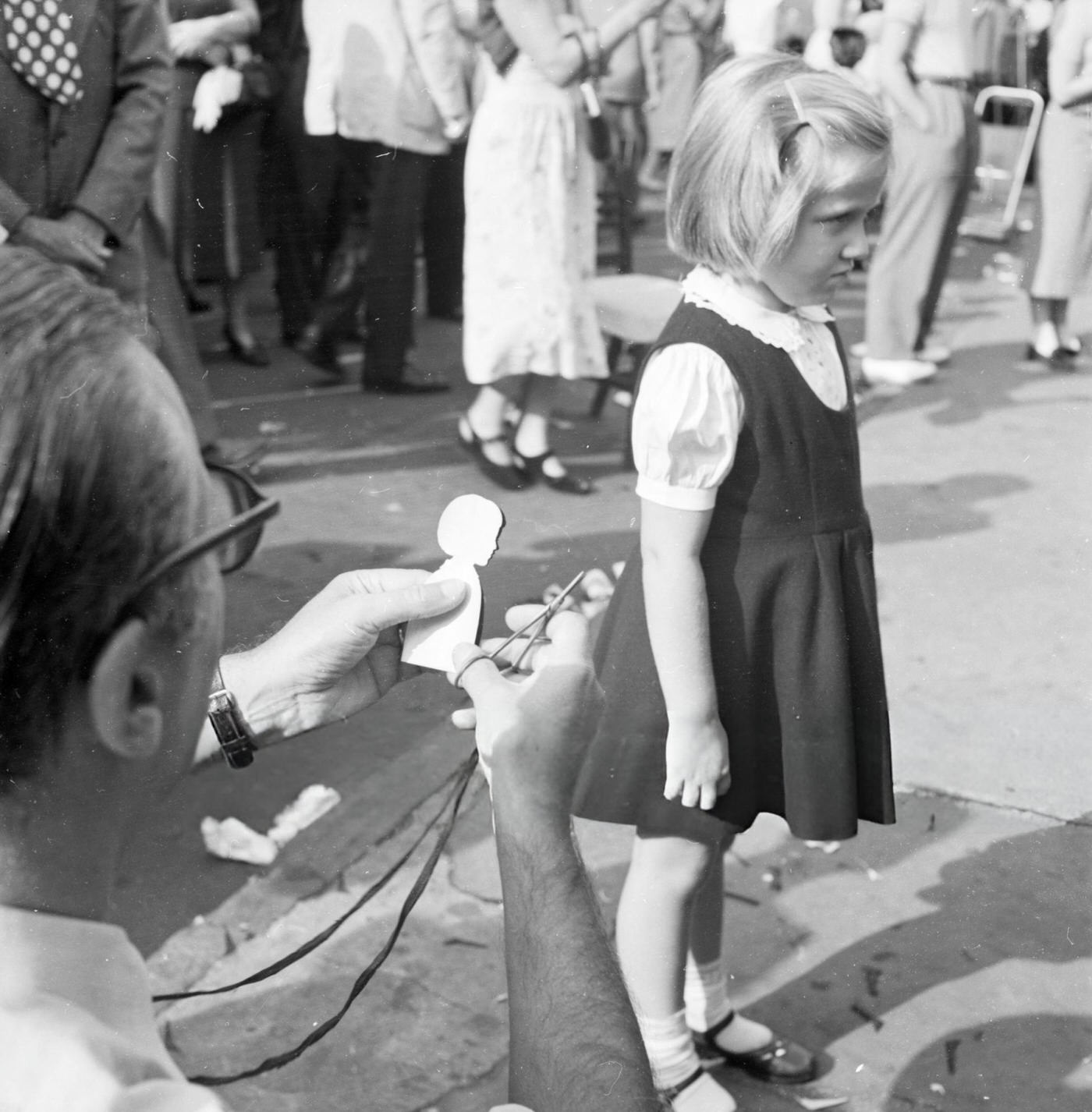 A street artist creates a cardboard silhouette of a little girl in Washington Square Park, 1955.