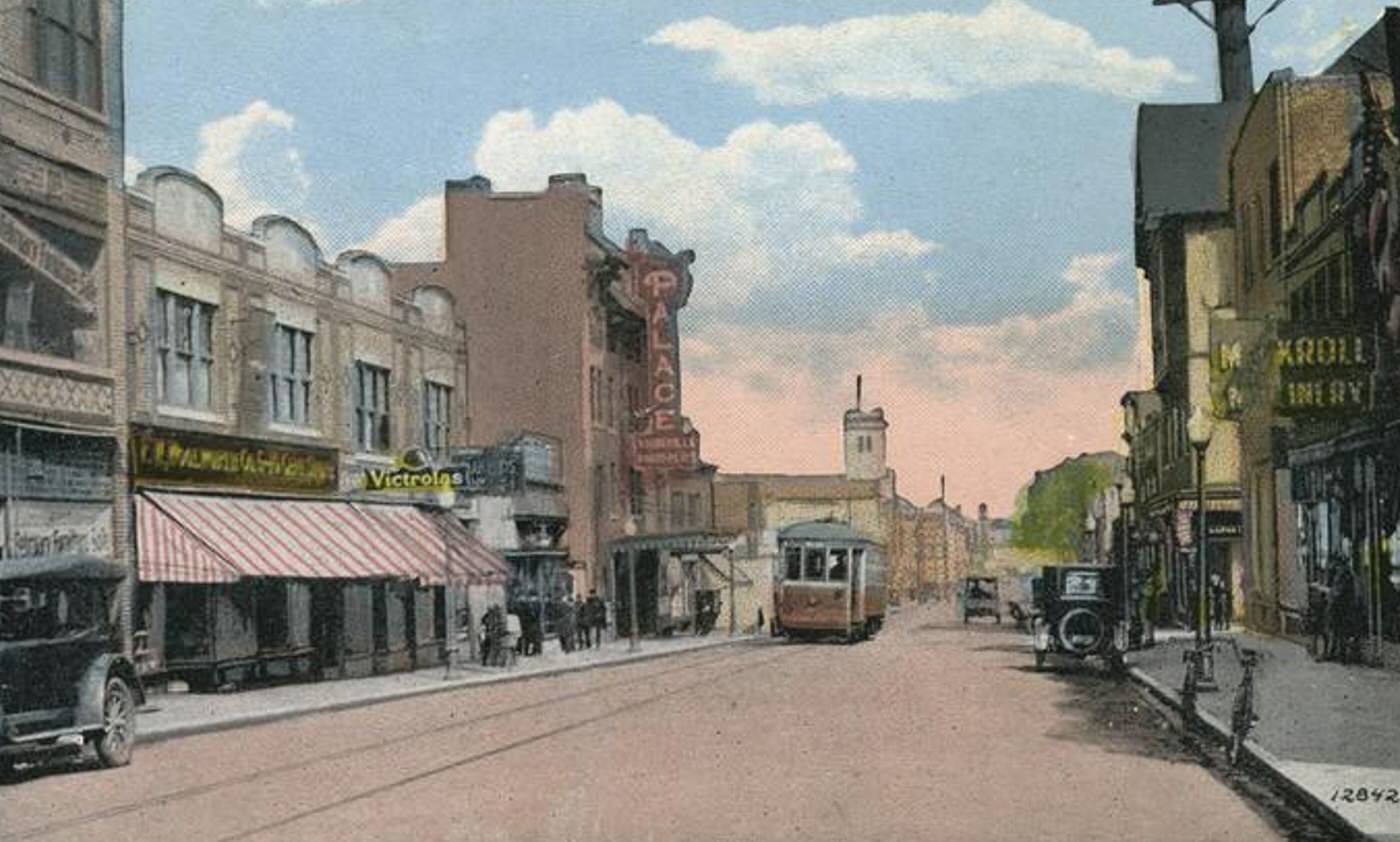 Richmond Ave. Port Richmond, featuring a trolley, old cars, people walking, and shops, 1900s.