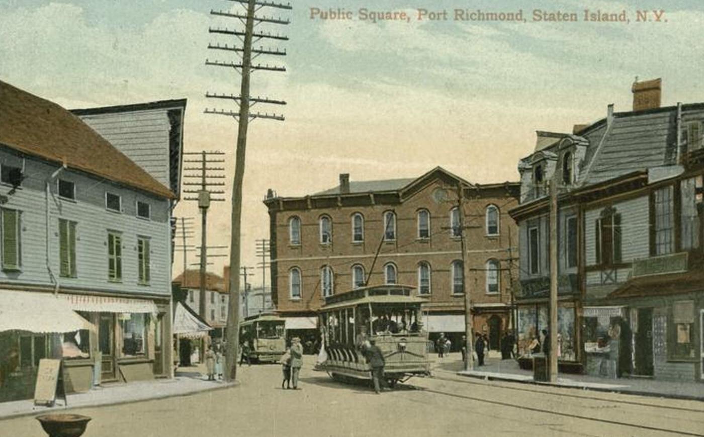 Public Square, Port Richmond, featuring a trolley loading people and shops on the street, 1900s.