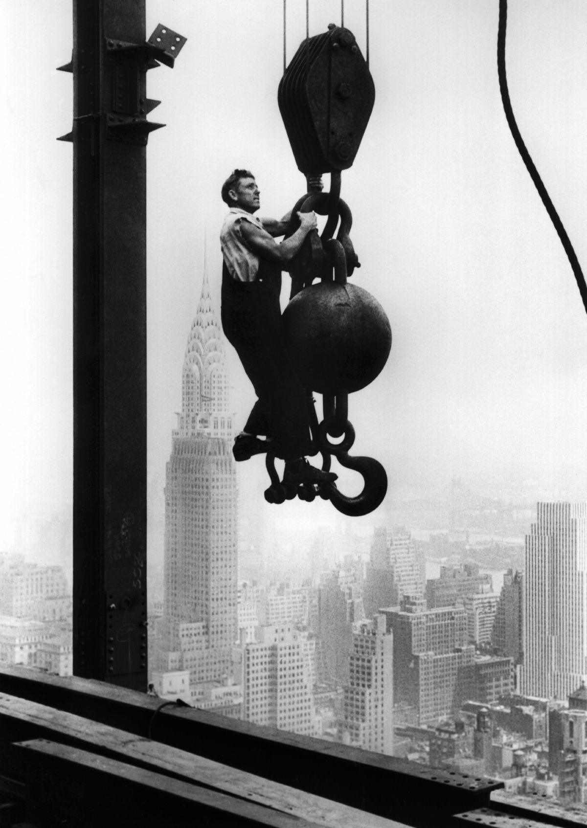 A construction worker hangs from an industrial crane during the construction of the Empire State Building, 1930.