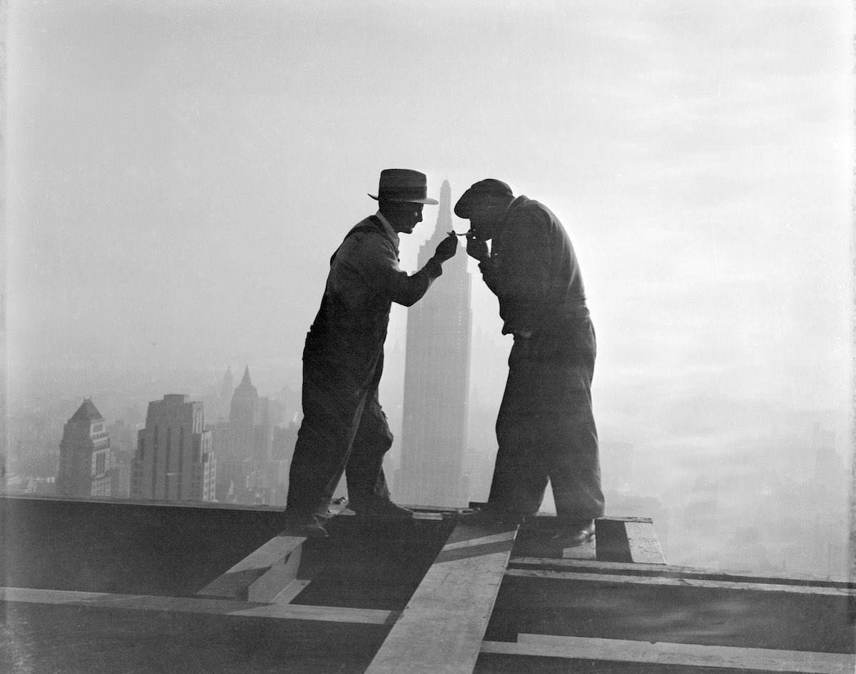 Workmen light their cigarettes atop the RCA Building in Rockefeller Center, with the Empire State Building in the background, 1932.