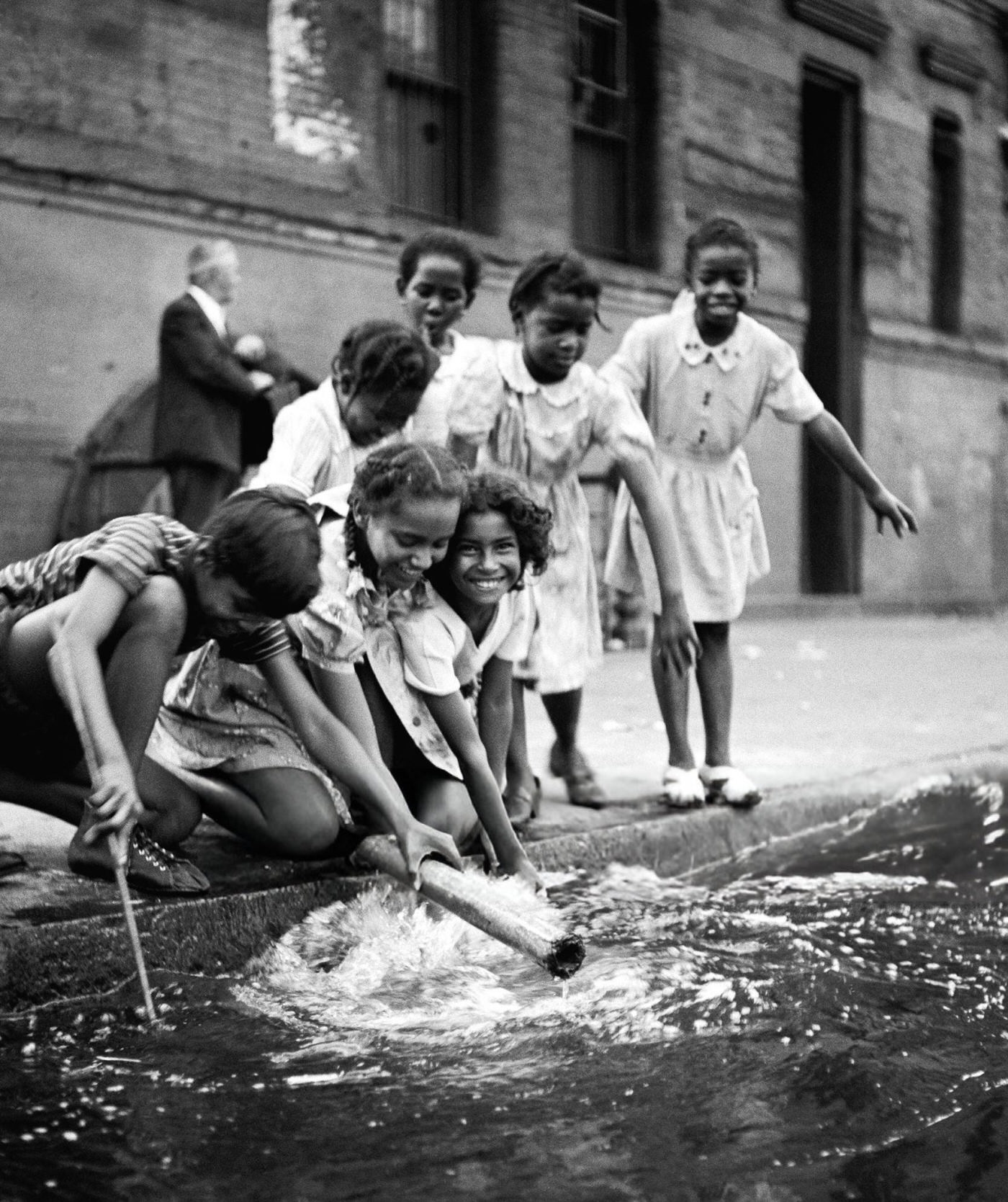 Young girls smile as they play beside a flooded street drain in Harlem, 1947.