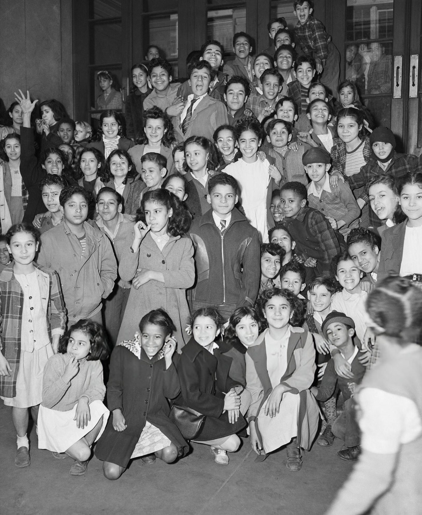 Group of Hispanic American and African American children stand on the steps of a Harlem elementary school, 1940s.