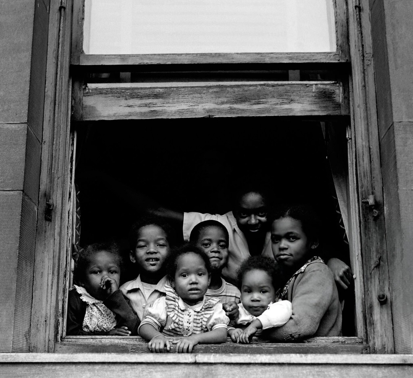 An African-American mother and her six children pose for a portrait out of their window in Harlem, 1948.