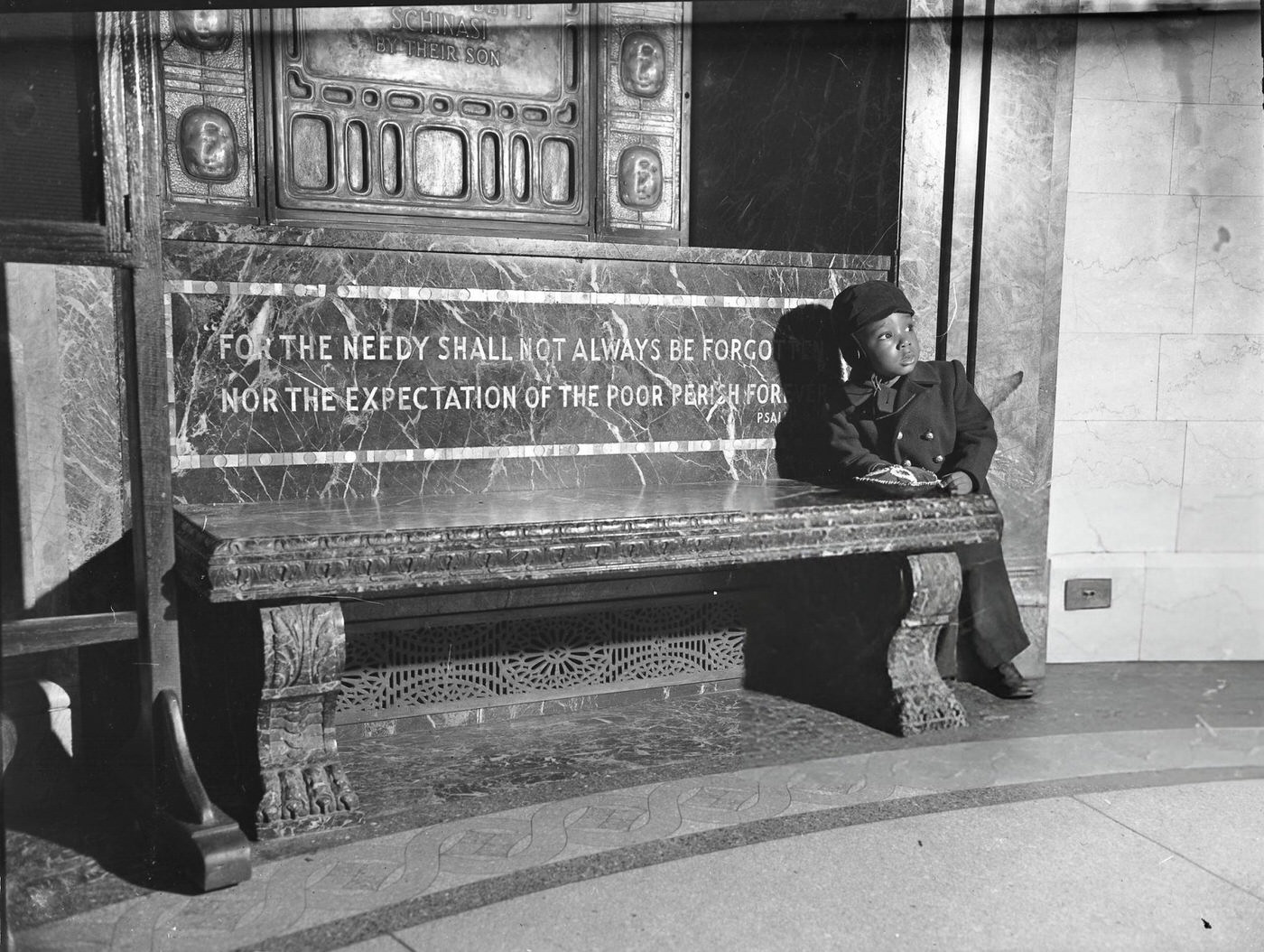 Young boy at Sydenham Hospital in Harlem, with text on the bench reading 'For the Needy Shall Not Always Be Forgotten', 1940s.