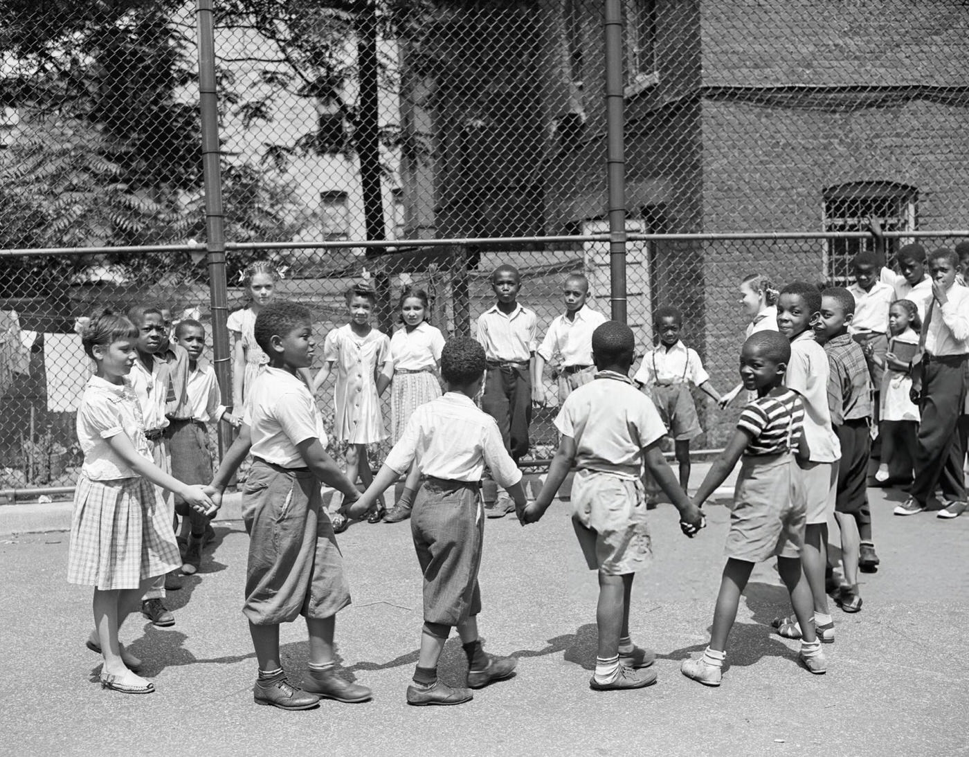 Black and white schoolchildren playing outside Harlem Public School No. 113 after graduation, 1943.