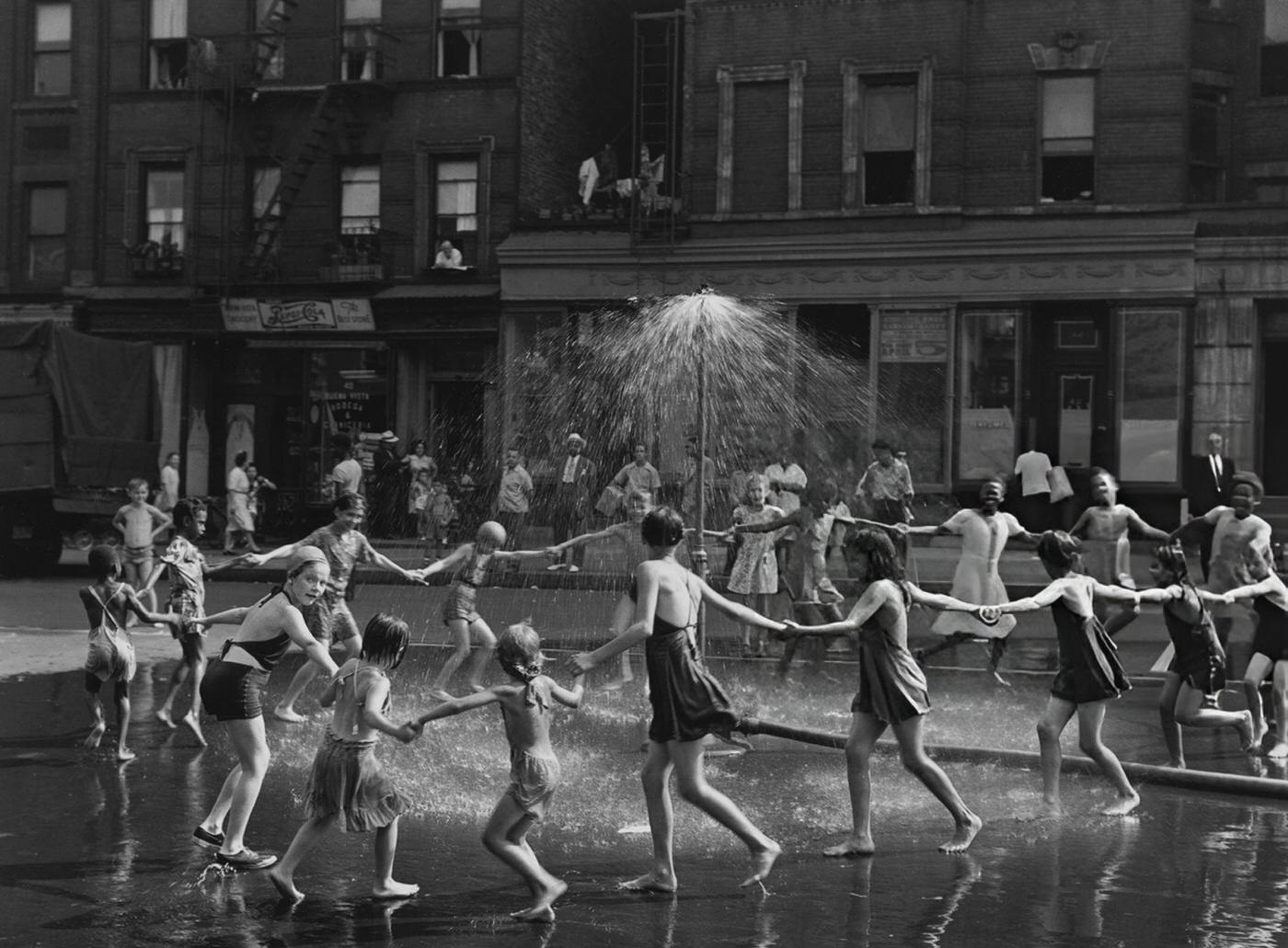 Children playing ring around the rosy around a sprinkler in Harlem, 1946.