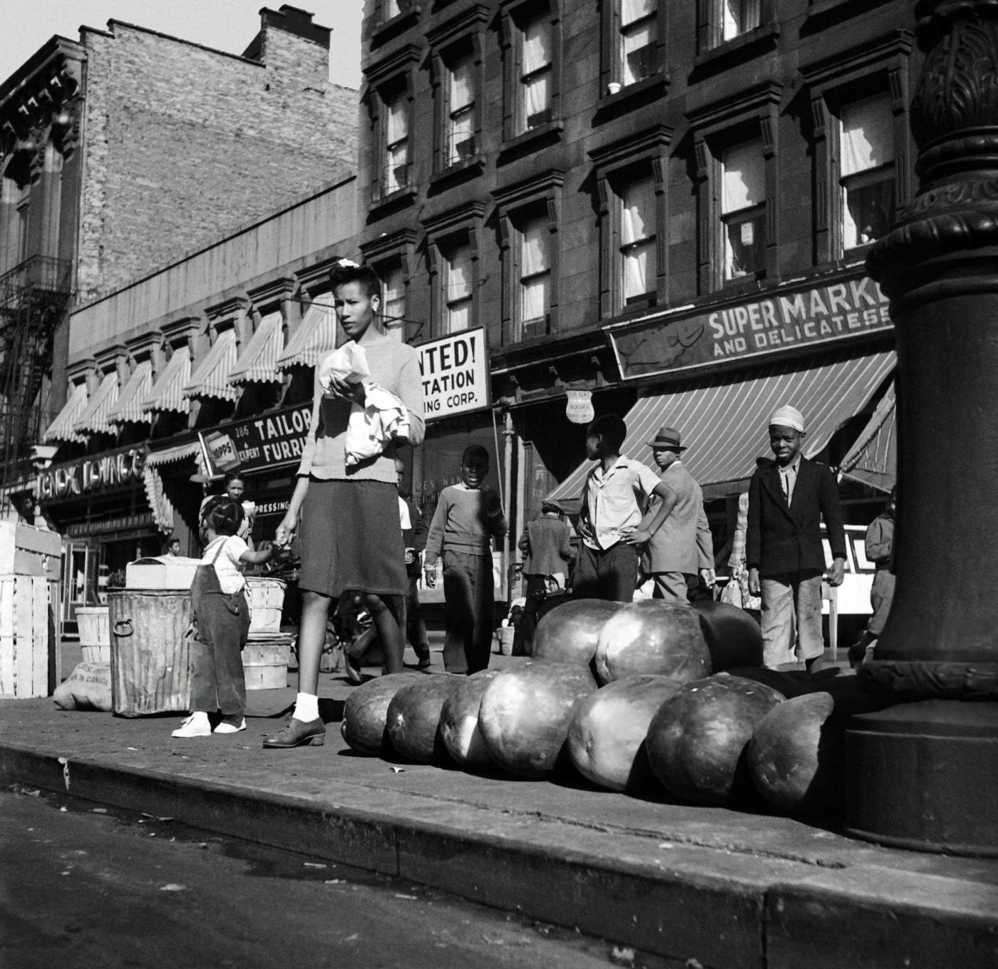 A woman and her child pass by watermelons on the sidewalk in Harlem, Manhattan, 1946.
