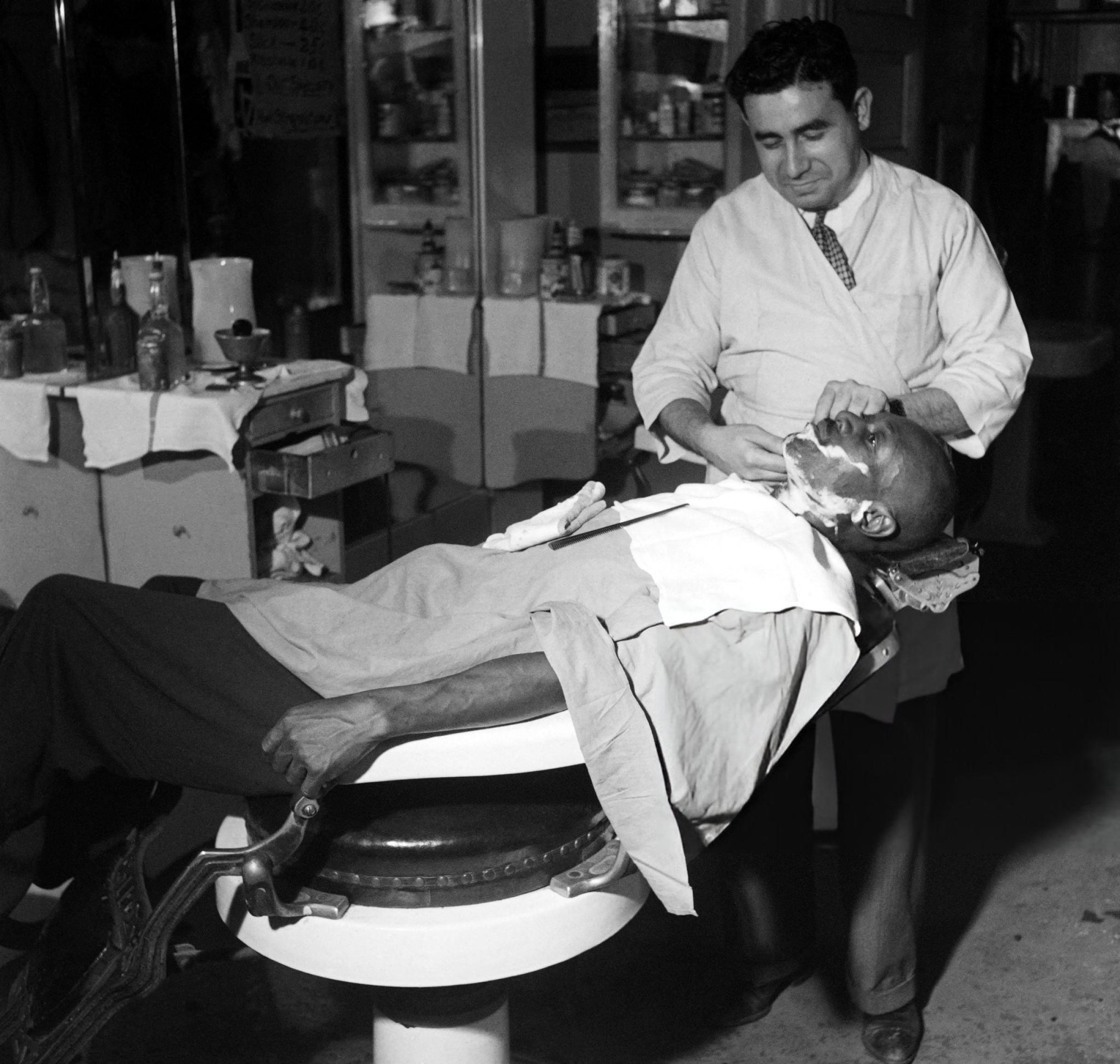 An African American man is shaved by an Italian barber in Harlem, Manhattan, 1946.