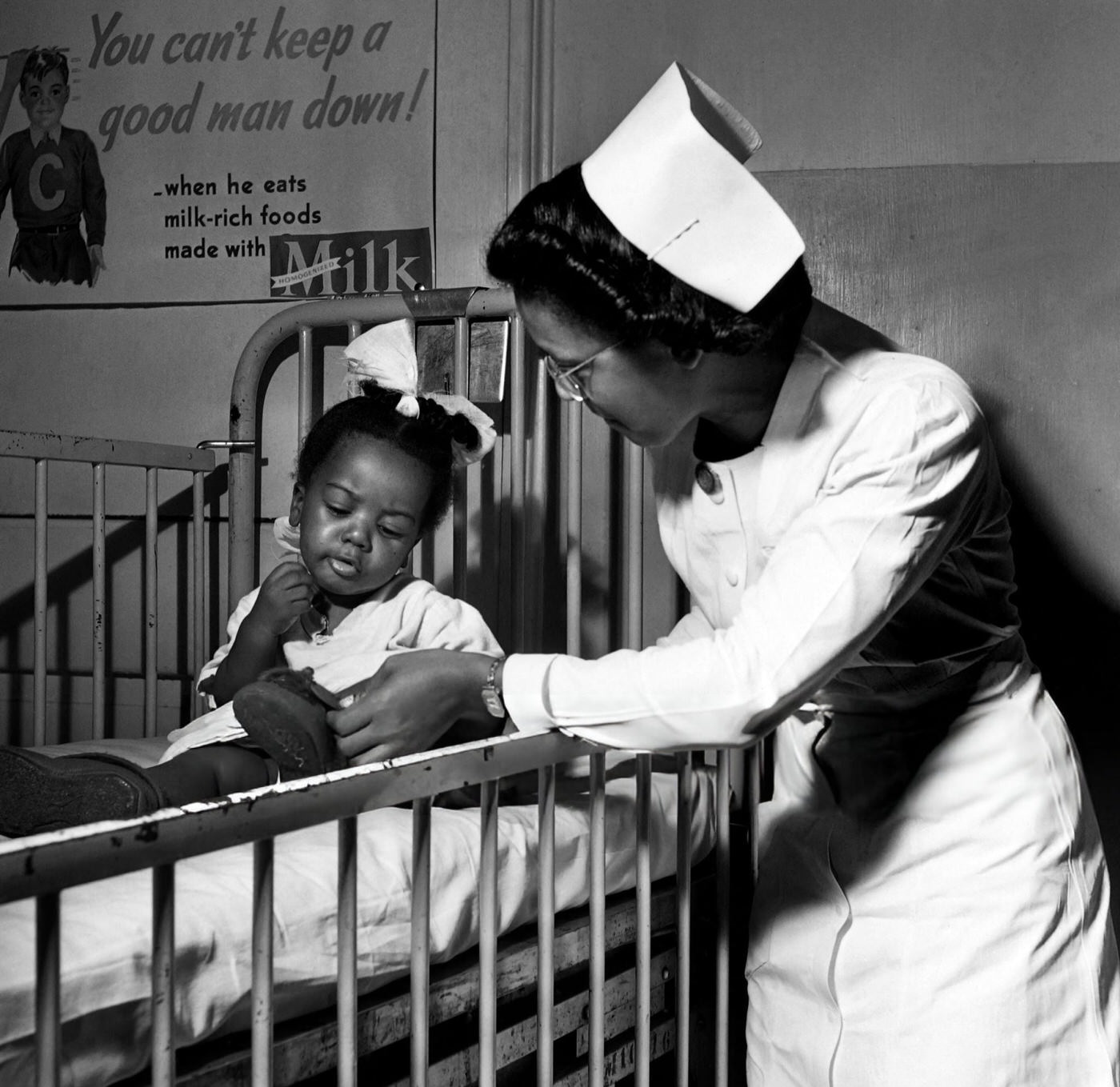 A nurse takes care of an African American little girl in a hospital nursery in Harlem, Manhattan, 1946.