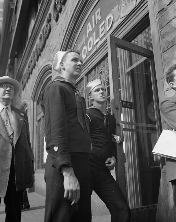 Two sailors smoke and lean, apprehensively scanning the latest news bulletins on the Times building.