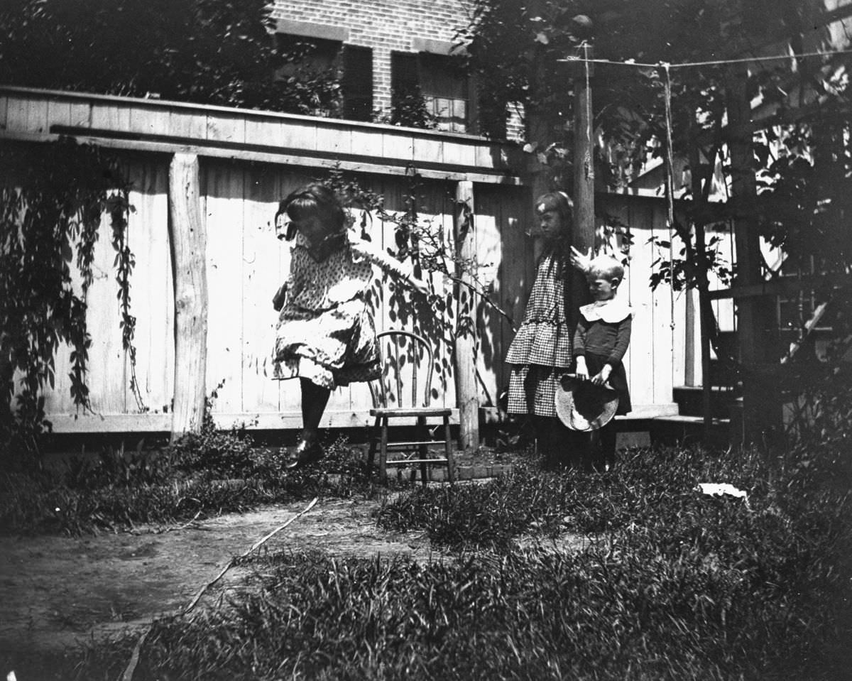 Mildred Grimwood jumps in the backyard at 314 Livingston Street as brother Victor Grimwood and pal Zelma Levison look on, 1886.