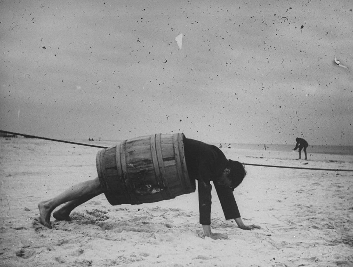A man in a barrel does a push up at the beach, 1880s