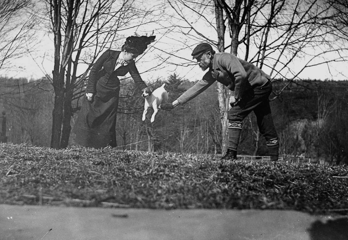 Dr. Ernest Palmer and wife join hands to make a bar so that their dog can jump over it.