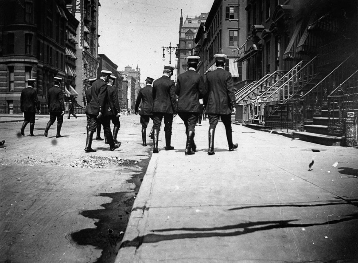 Uniformed officers in riding boots walk down a street, 1886.