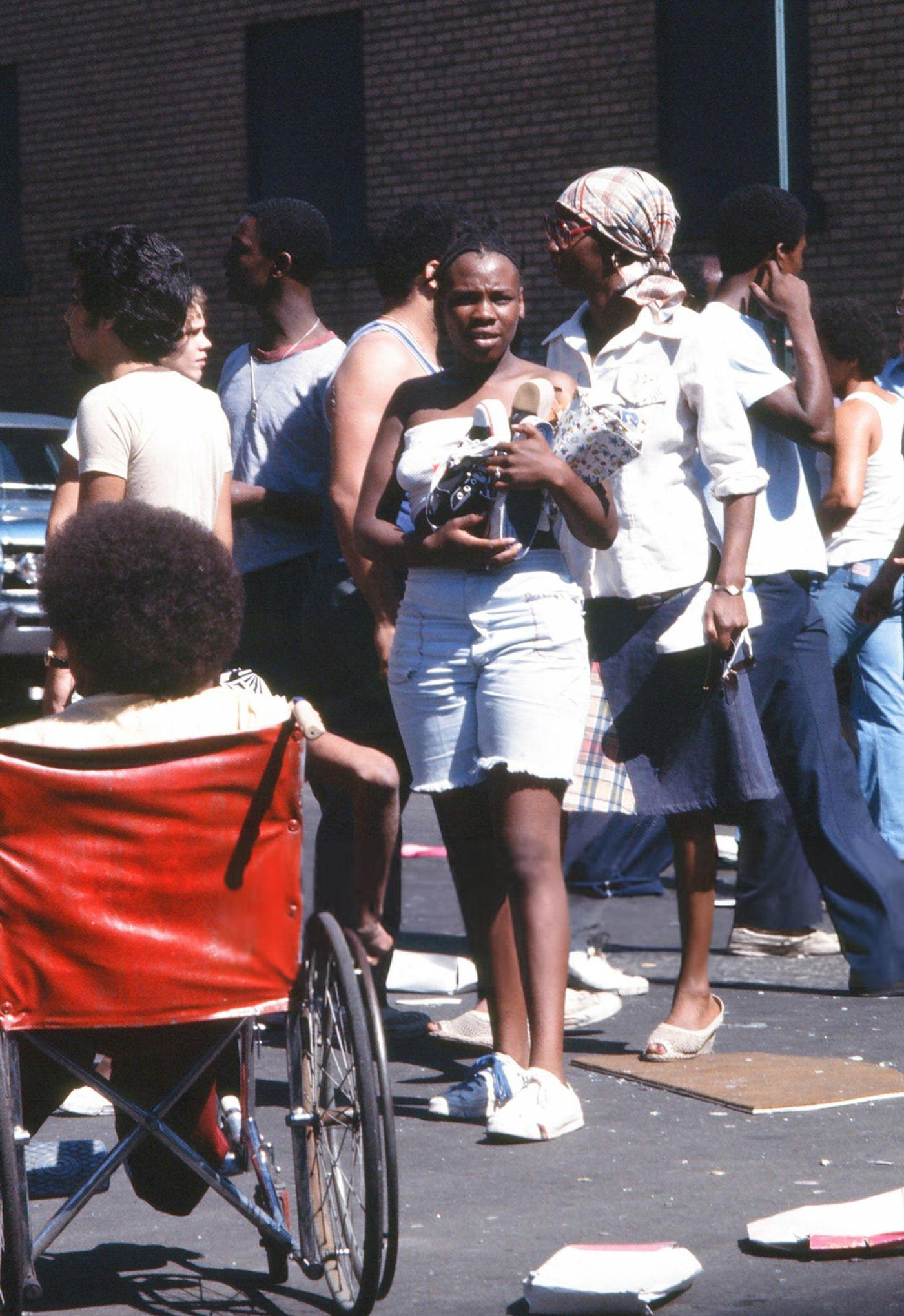 Passersby stand in front of a damaged store front, looted during the New York City blackout, Brooklyn, 1977.
